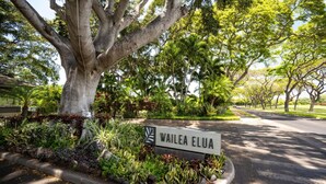 Un panneau indiquant « WAILEA ELUA », placé dans un espace paysager agrémenté d’arbres et de plantes.
