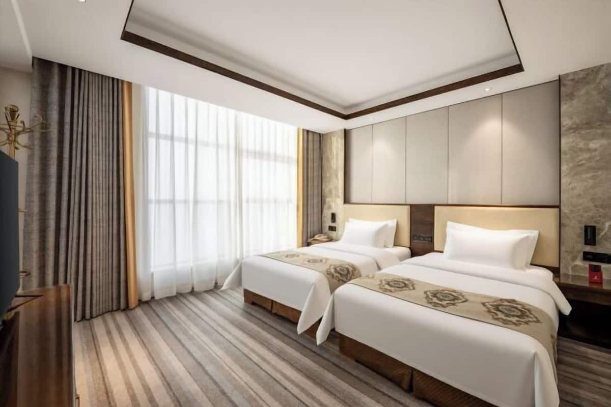Habitación de hotel con dos camas, un ventanal grande con cortinas, piso de madera y un diseño moderno en el techo.