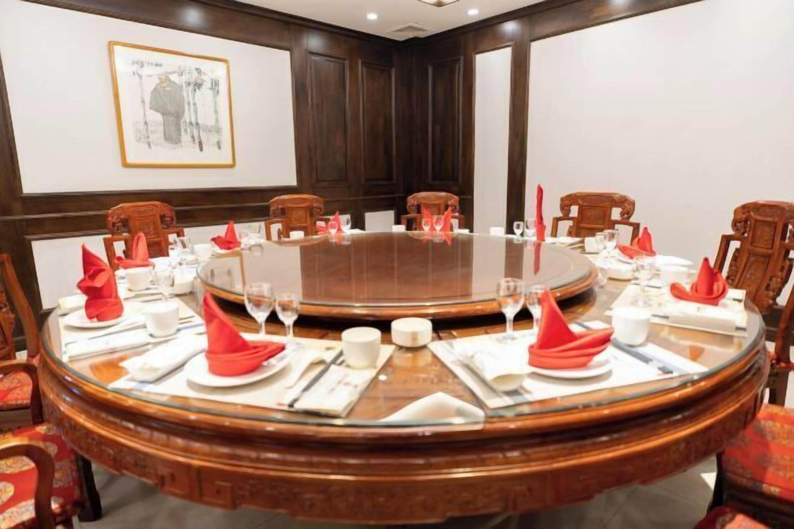 Een vergaderruimte met een ronde glazen tafel, houten stoelen en rode servetten.