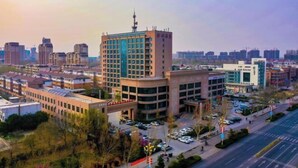 A modern urban area with a prominent multi-story building featuring a central tower with a satellite dish. - Jinshui Hot Spring Hotel (Shen County)