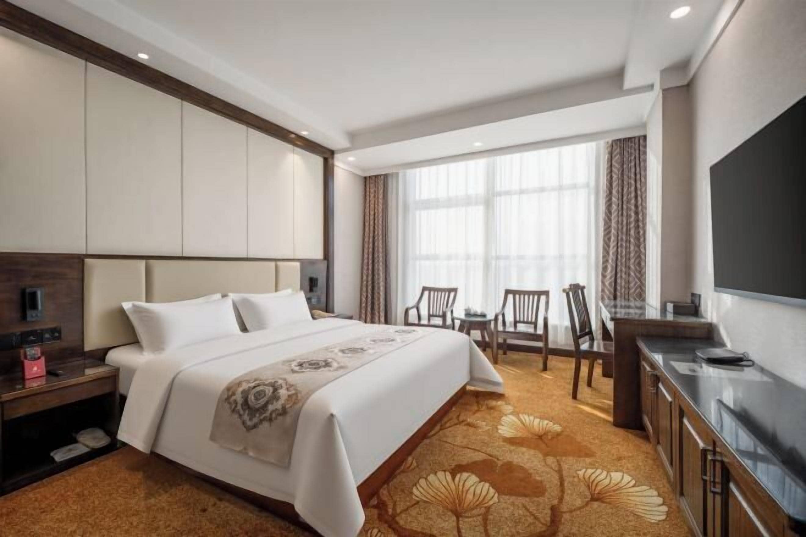 A hotel room with a bed, a desk, a TV, and a window with curtains.