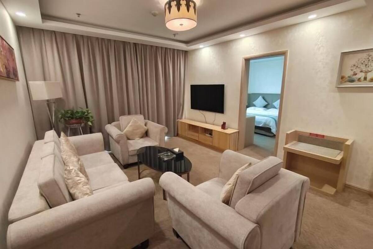 Habitación de hotel moderna con sofá, televisor de pantalla plana, una mesita y cama con cabecero.