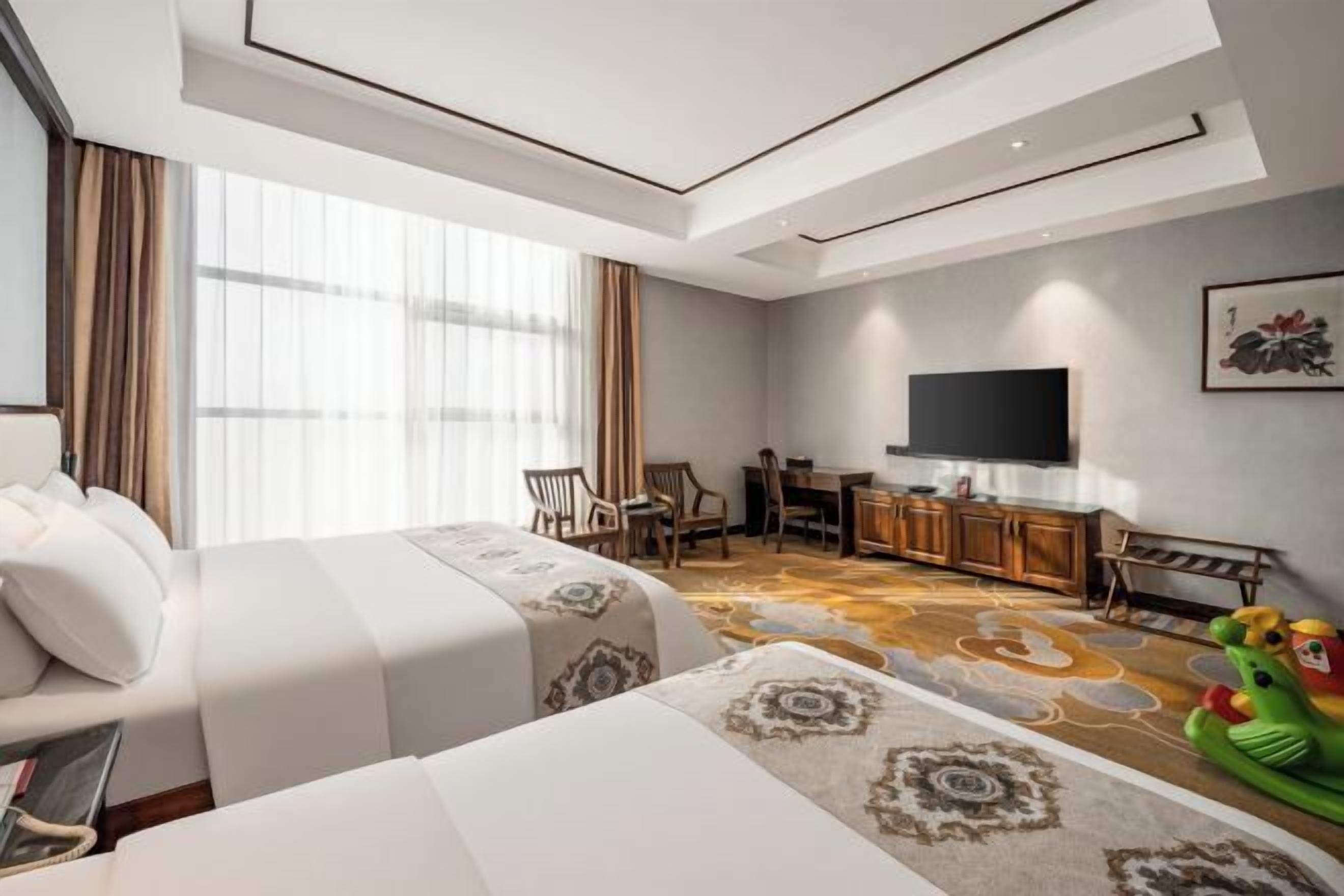 A hotel room with a large bed, a desk, a chair, a television, and a dining area.