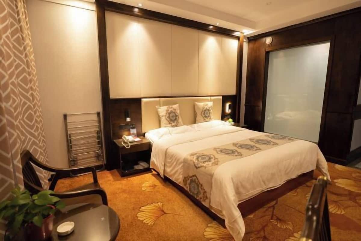 Una habitación de hotel con cama, mesita de noche, silla y un ventanal grande.