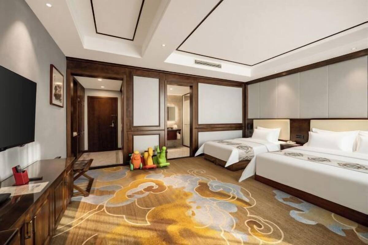 Habitación de hotel con dos camas, un escritorio, un televisor y una alfombra colorida.