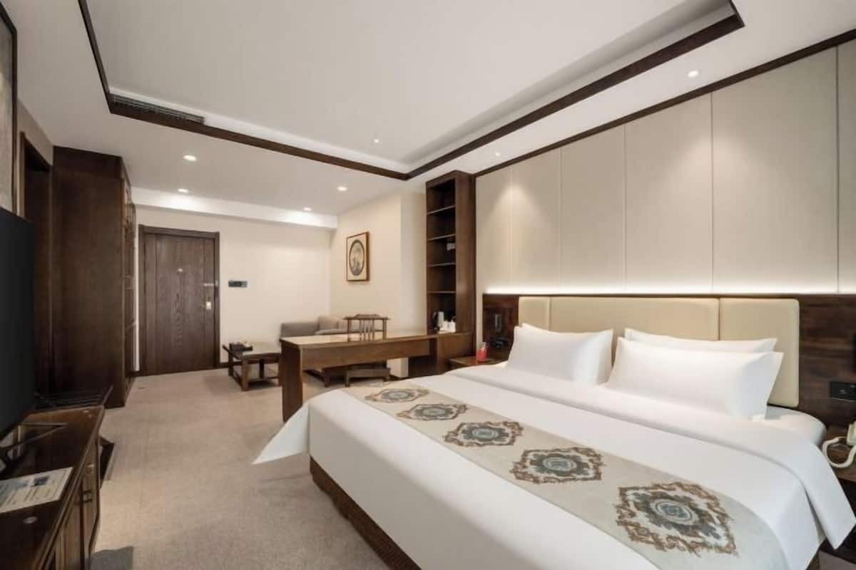 Habitación de hotel con una cama grande, escritorio, silla, televisor y armarios empotrados.