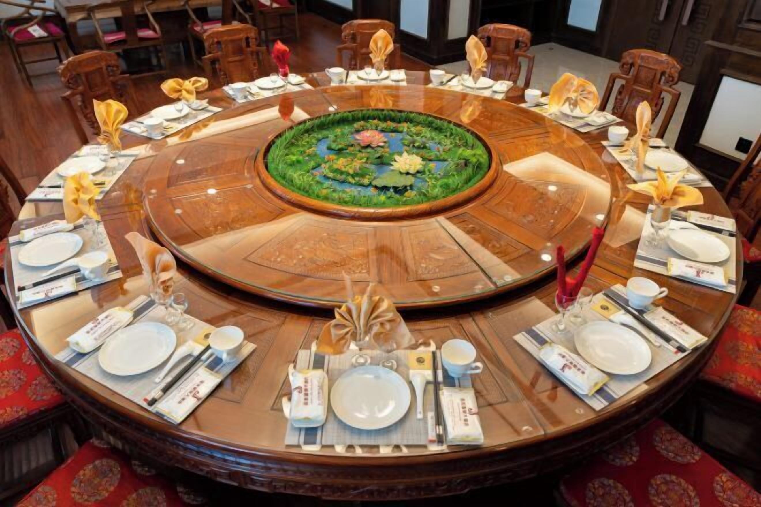 Une table de salle à manger ronde, agrémentée d’un arrangement floral au centre, entourée de chaises et dressée avec des assiettes, des verres et des couverts.