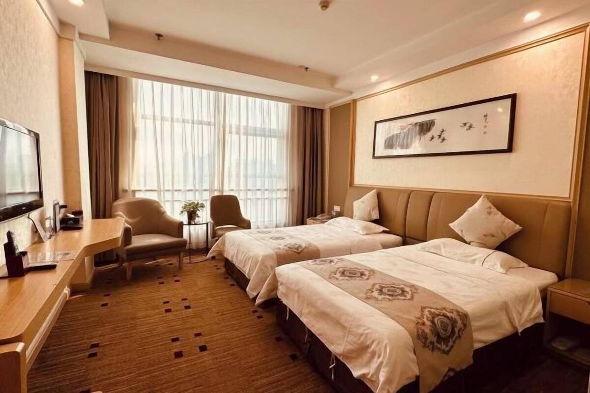 Una habitación de hotel con dos camas, un escritorio, una silla y un ventanal con cortinas.