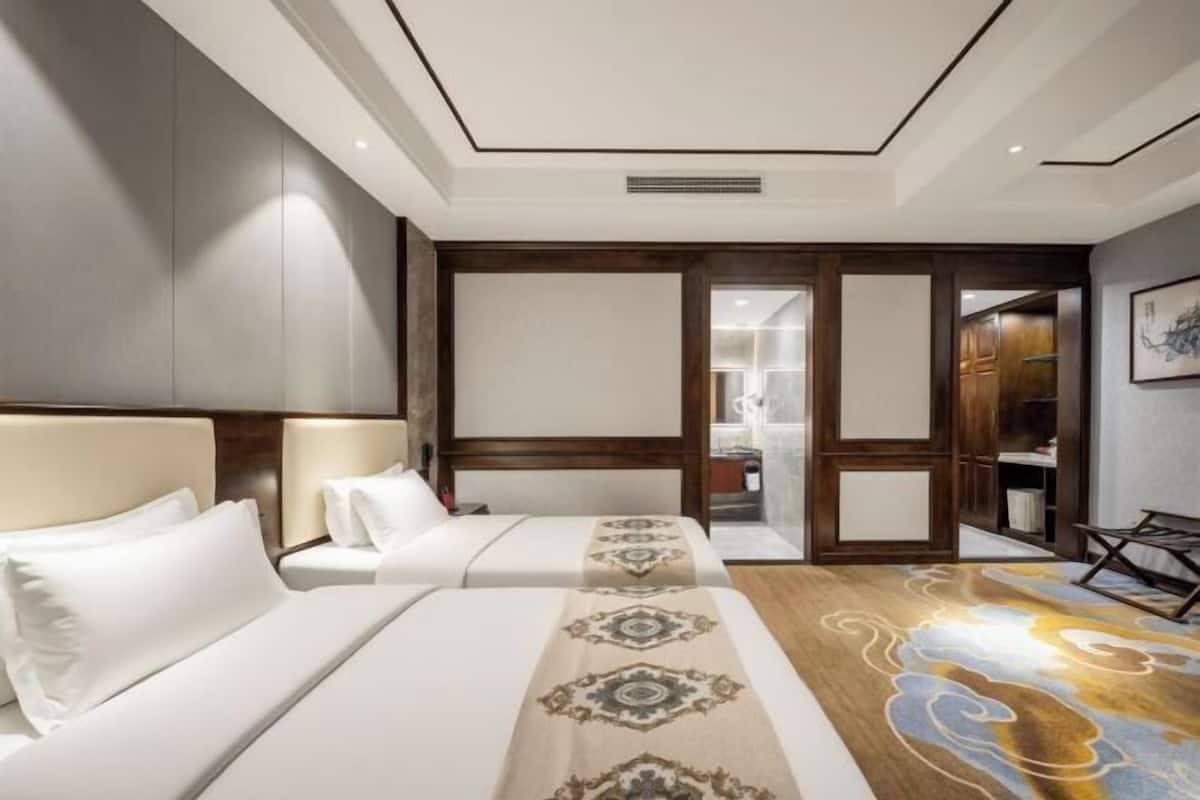 Habitación de hotel con dos camas, suelo de madera, un espejo grande y vistas a la cocina.