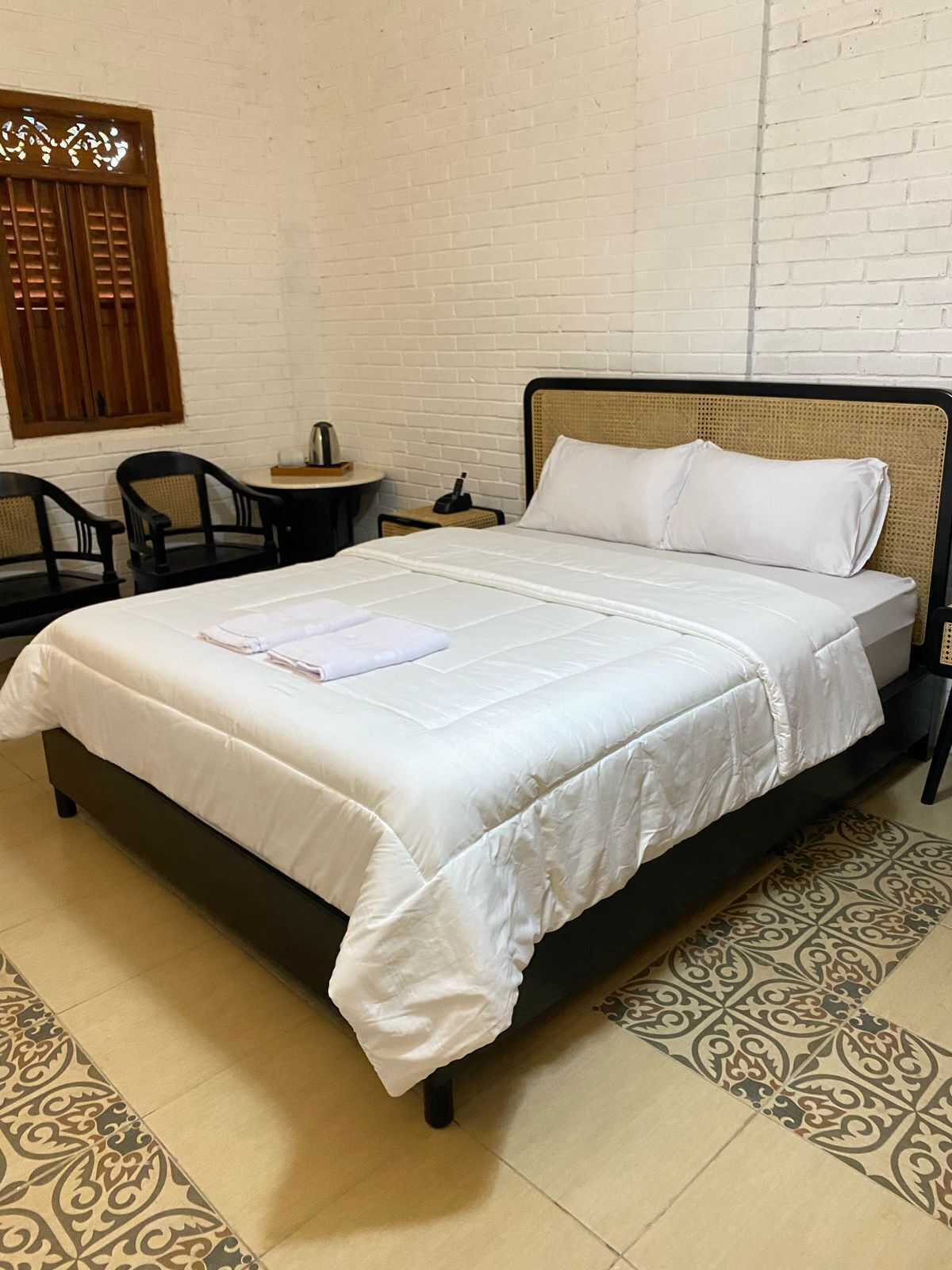 A neatly made bed with white linens, a small bedside table with a lamp, and a chair.