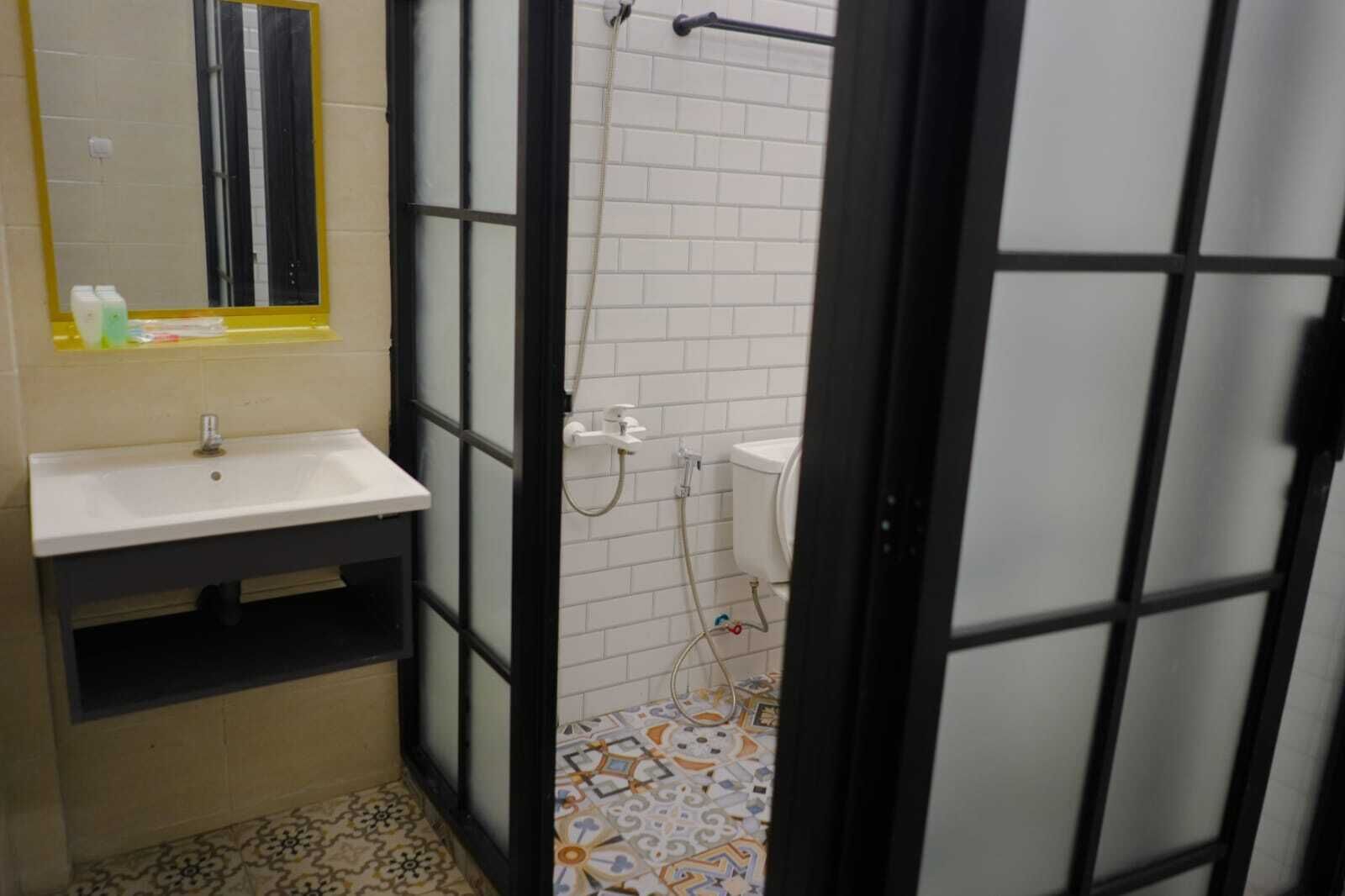 A bathroom with a white sink, mirror, and toilet. The floor has patterned tiles, and there is a shower area visible through a glass door.