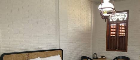A single bed with a white mattress and headboard, a small table with chairs, and a hanging light fixture.