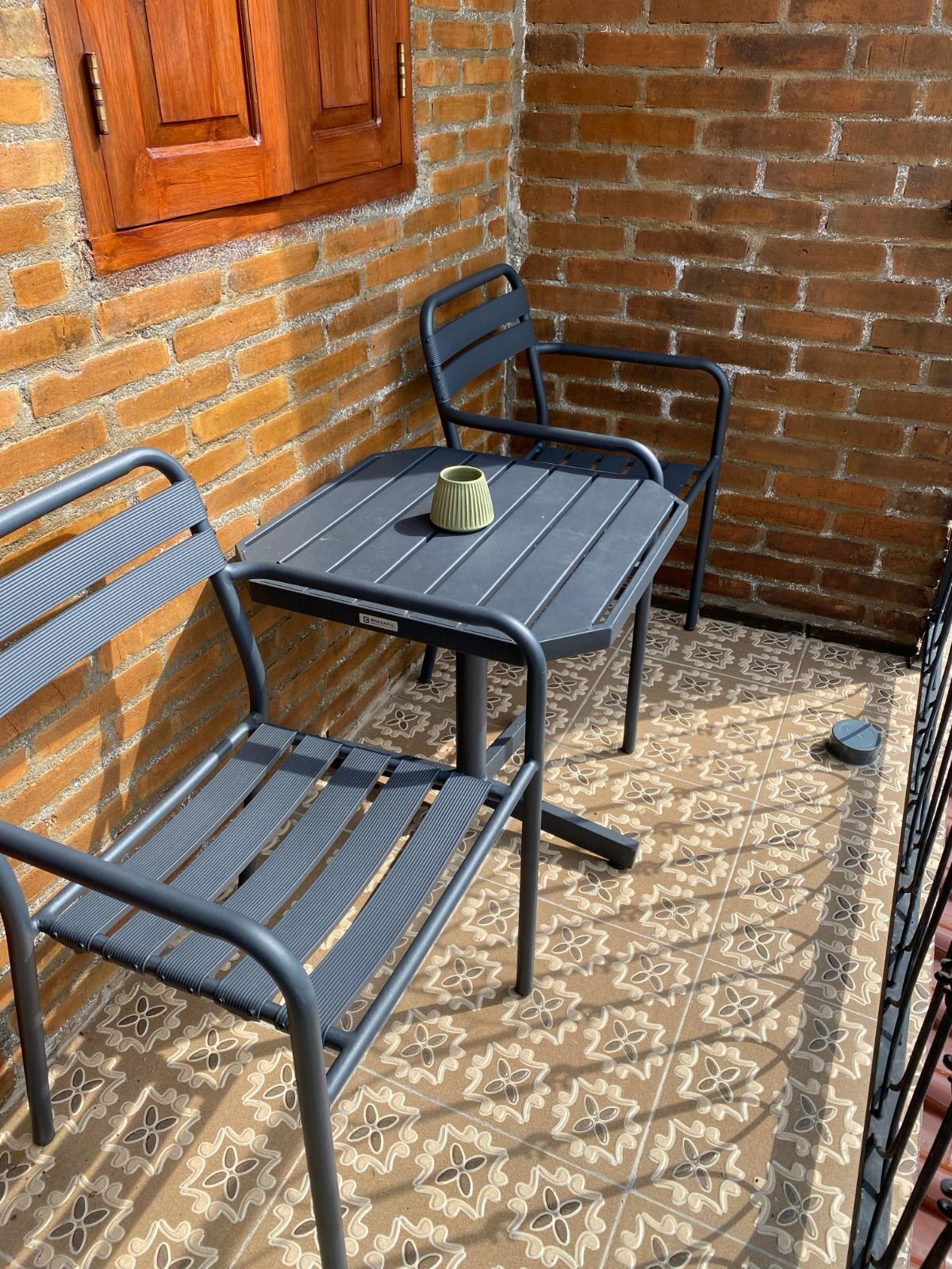 Un patio con pared de ladrillo, puerta de madera y mesa con dos sillas.