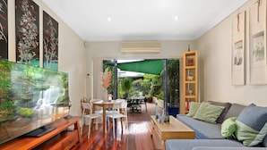 A modern living room with a TV, wooden furniture, a sofa, and a dining area with chairs and a table.