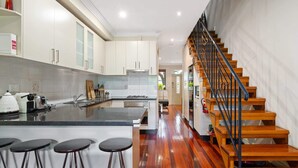 A modern kitchen with a central island, wooden staircase, and a view into the living area.
