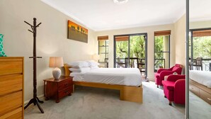 A bedroom with a bed, a nightstand, a lamp, a coat rack, and a window with a view of trees.
