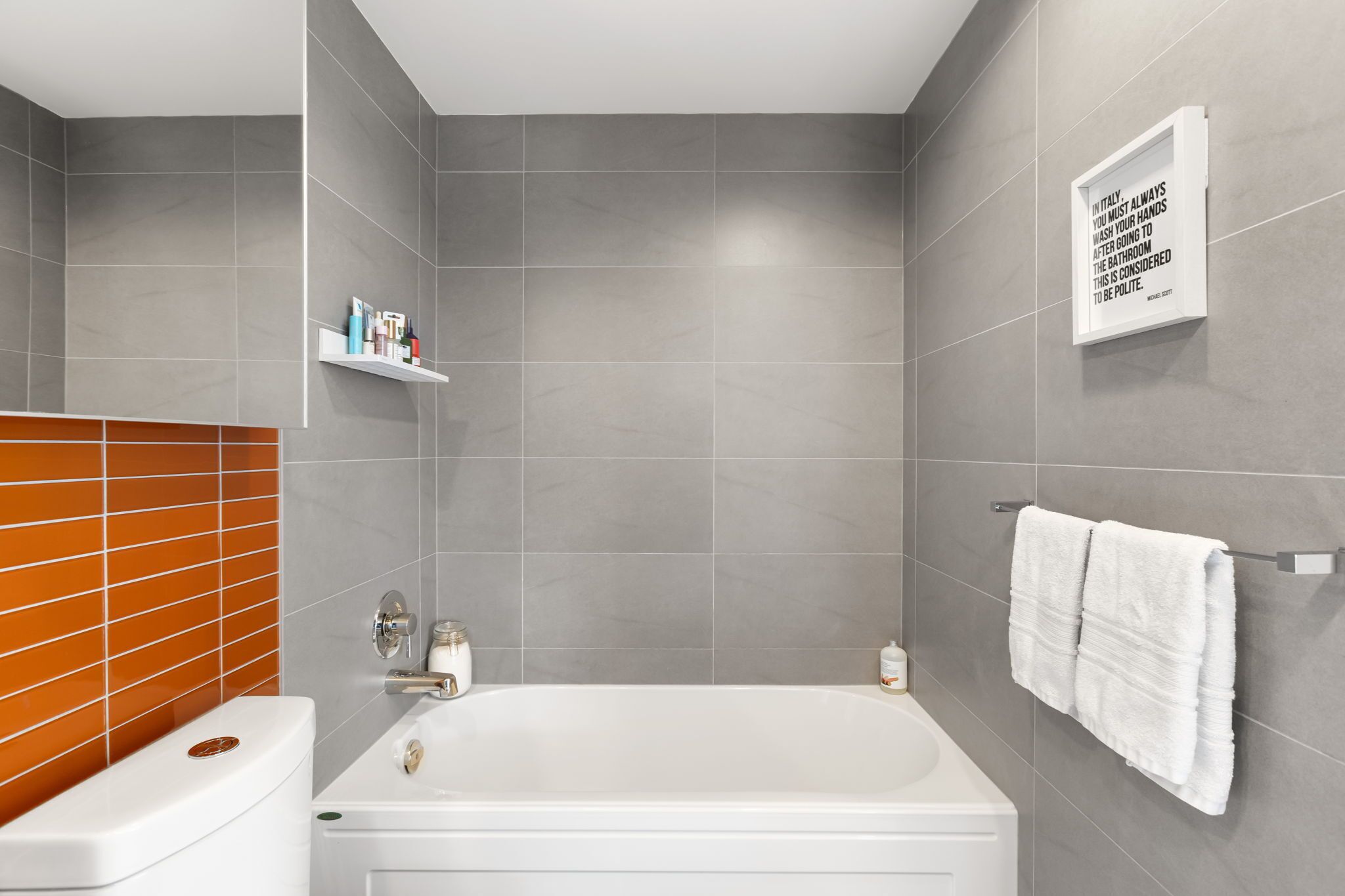 A modern bathroom with a bathtub, a toilet, and a shelf with toiletries.