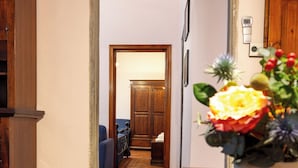 A hallway with a wooden table and a vase of flowers. There is a blue couch and a wooden cabinet in the background. - Romantic and TYPICAL FLORENTINE APARTMENT a 5min da Ponte Vecchio e Pitti Palace (Firenze)