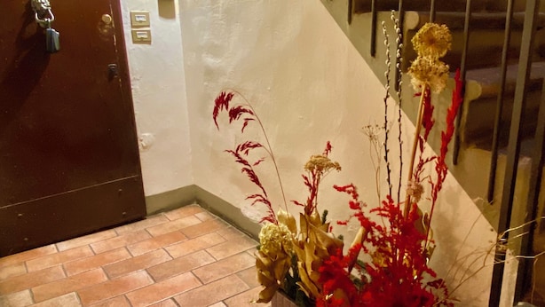 A staircase with metal railings, a brown door, and a potted plant with red and yellow flowers on a tiled floor. - Romantic and TYPICAL FLORENTINE APARTMENT a 5min da Ponte Vecchio e Pitti Palace (Firenze)