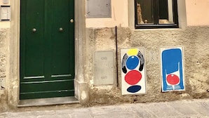 A building with a green door, a window with a metal grate, and two colorful signs on the wall. - Romantic and TYPICAL FLORENTINE APARTMENT a 5min da Ponte Vecchio e Pitti Palace (Firenze)