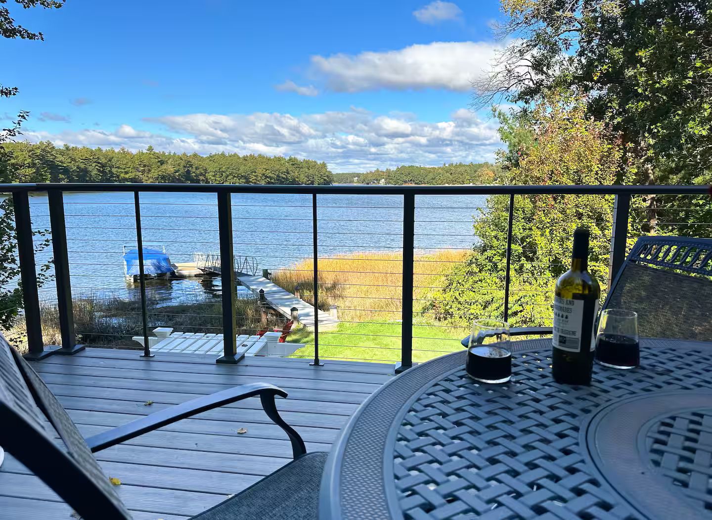 A balcony with a view of a lake, a bottle of wine, and a glass on a table.