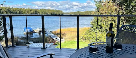 A balcony with a view of a lake, a bottle of wine, and a glass on a table.