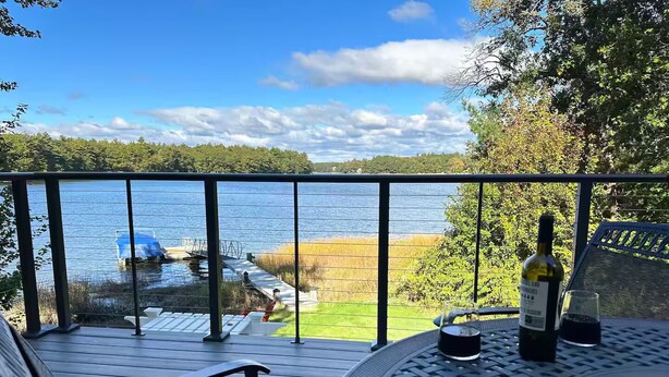 A balcony with a view of a lake, a bottle of wine, and a glass on a table. - Waterfront Oasis~Pool Table~Deck~Dock~Garage (Dover)