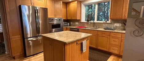 A kitchen with wooden cabinets, a stainless steel refrigerator, an oven, and a window with a view of trees.