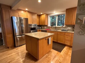 A kitchen with wooden cabinets, a stainless steel refrigerator, an oven, and a window with a view of trees. - Waterfront Oasis~Pool Table~Deck~Dock~Garage (Dover)