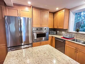 A kitchen with stainless steel appliances, wooden cabinets, a granite countertop, and a window with a view of trees. - Waterfront Oasis~Pool Table~Deck~Dock~Garage (Dover)