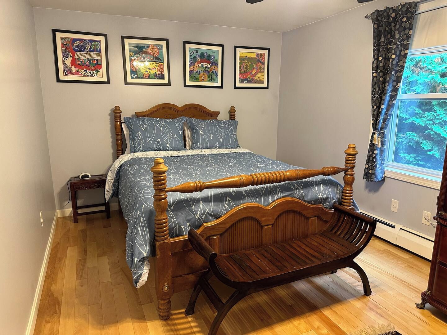 Une chambre à coucher avec un lit à baldaquin en bois, une chaise en bois, une table de chevet et trois œuvres d’art encadrées accrochées au mur.