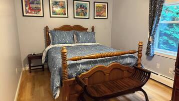 Une chambre à coucher avec un lit à baldaquin en bois, une chaise en bois, une table de chevet et trois œuvres d’art encadrées accrochées au mur.
