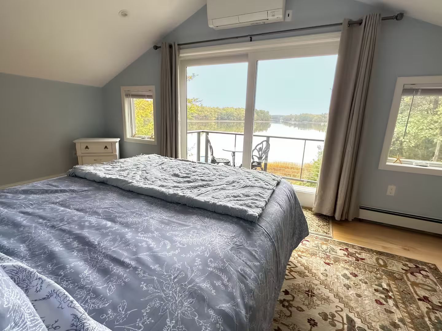 Un dormitorio con una cama grande, vistas a un lago y un balcón con una silla.