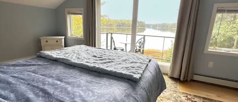 Un dormitorio con una cama grande, vistas a un lago y un balcón con una silla.