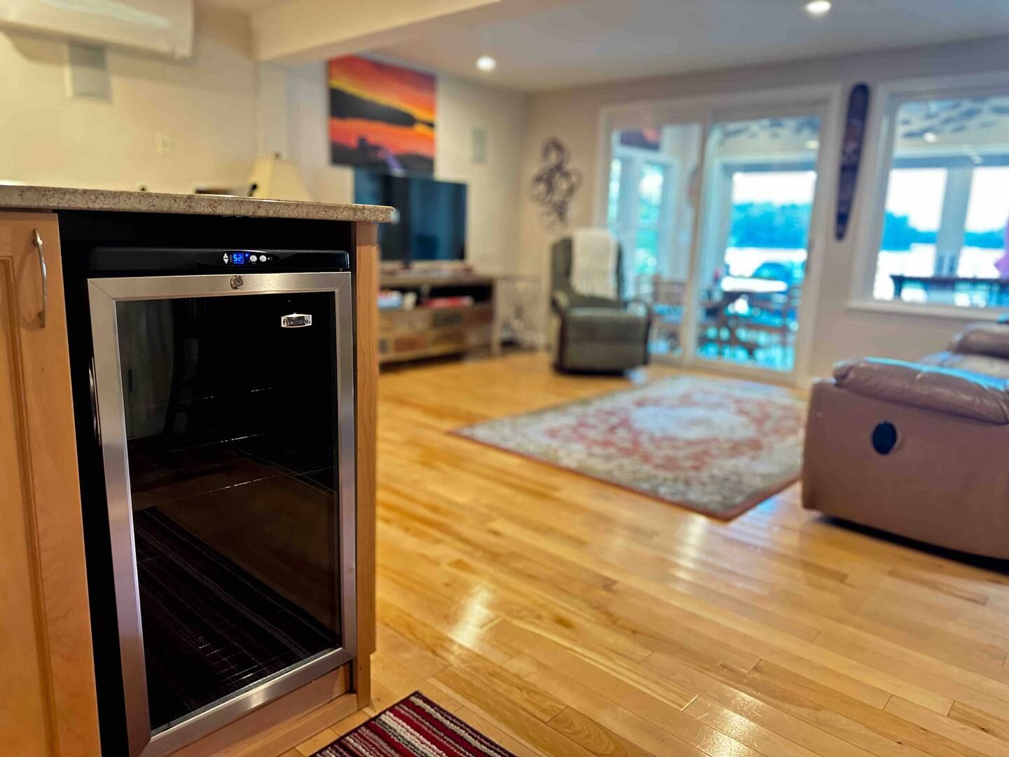 A kitchen with a built-in oven, wooden flooring, a rug, and a view through the glass door.
