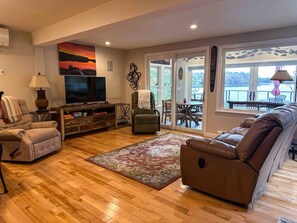 A living room with a television, sofa, armchair, and a view of the outdoors through a sliding glass door. - Waterfront Oasis~Pool Table~Deck~Dock~Garage (Dover)