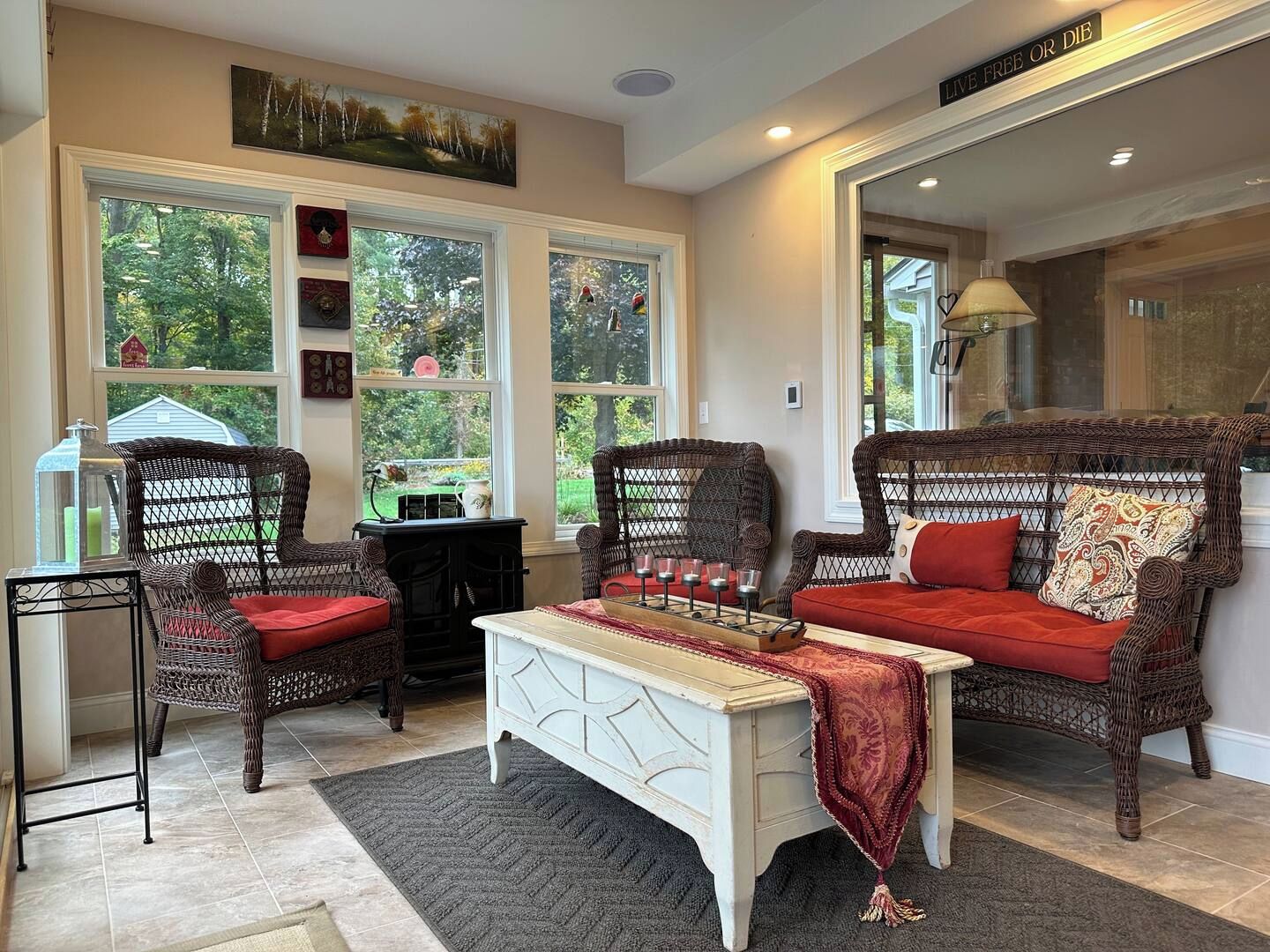 A cozy living room with wicker furniture, a white coffee table, and large windows offering a view of the outdoors.