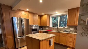 A kitchen with wooden cabinets, a stainless steel refrigerator, an oven, and a window with a view of trees. - Waterfront Oasis~Pool Table~Deck~Dock~Garage (Dover)