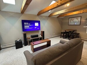A living room with a flat-screen TV, wooden beams, a sofa, a coffee table, and a dining area with a map on the wall. - Waterfront Oasis~Pool Table~Deck~Dock~Garage (Dover)