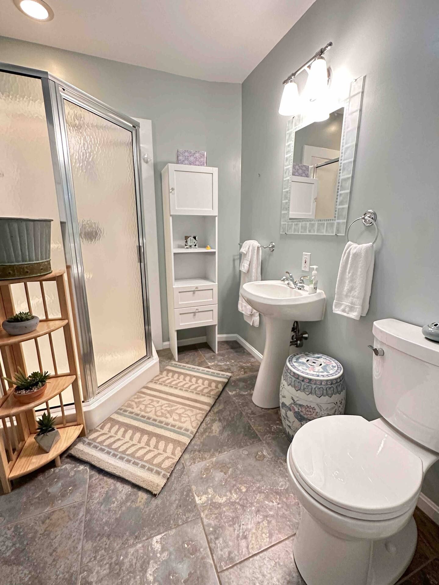 A bathroom with a shower, sink, toilet, and a mirror.