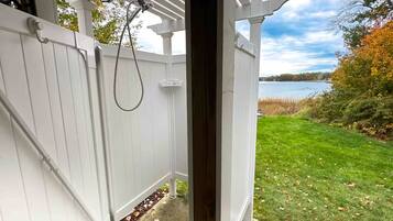 A white wooden pergola with a hose attached, overlooking a grassy yard with a body of water in the background.