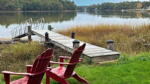 A wooden dock extending into a calm lake, with red Adirondack chairs on the grass near the dock. - Waterfront Oasis~Pool Table~Deck~Dock~Garage (Dover)