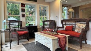A cozy living room with wicker furniture, a white coffee table, and large windows offering a view of the outdoors. - Waterfront Oasis~Pool Table~Deck~Dock~Garage (Dover)
