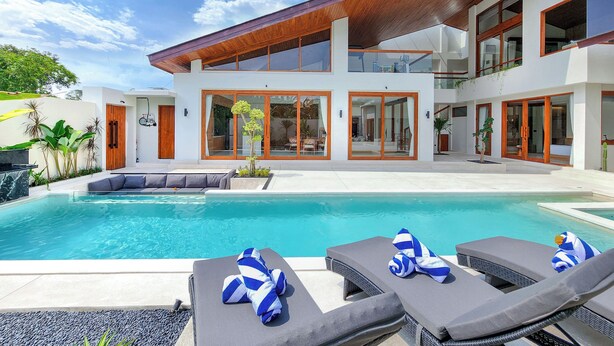 A modern house with a swimming pool, lounge chairs, and a wooden deck.