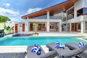 A modern house with a swimming pool, lounge chairs, and a wooden deck. - The Aurum Canggu Villas by Nagisa Bali (Canggu)