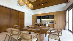 Una cocina moderna con armarios de madera, un comedor con una gran mesa de madera y sillas de mimbre, y luces colgantes.