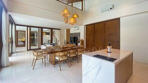 A spacious dining area with a marble island, wooden chairs, and woven pendant lights.
