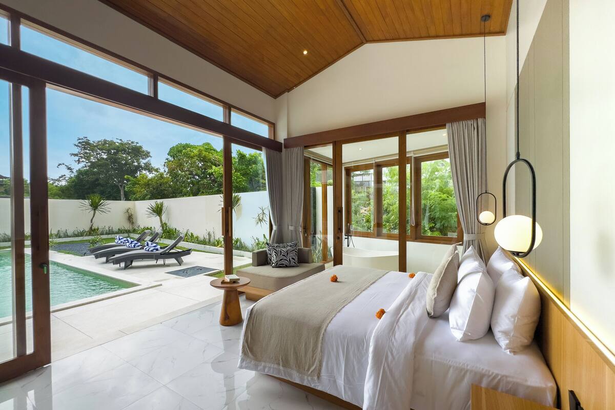 A spacious bedroom with a large bed, a view of the pool, and a balcony.