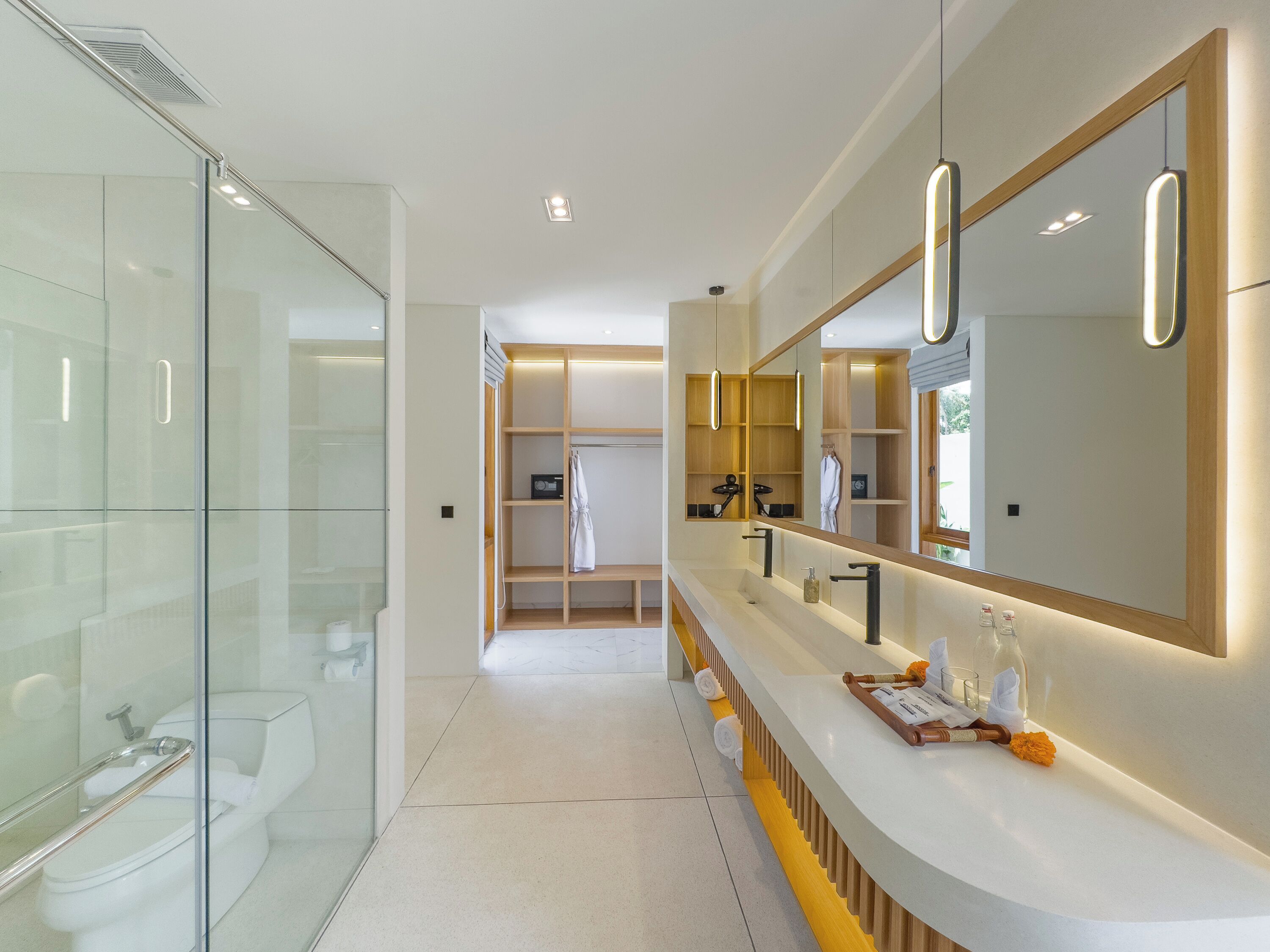 A modern bathroom with a glass shower enclosure, a vanity with a large mirror, and a walk-in closet with shelves.