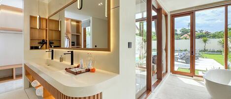 A modern bathroom with a large mirror, a bathtub, and a view of a pool and garden.
